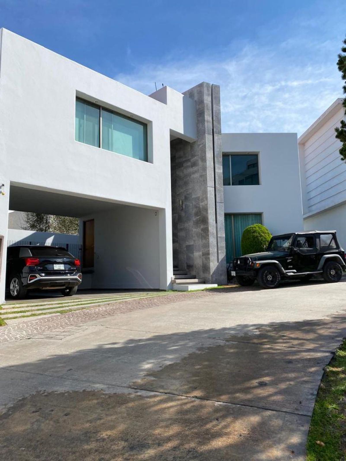 Fachada moderna de casa blanca con columna de piedra gris, grandes ventanas y cochera