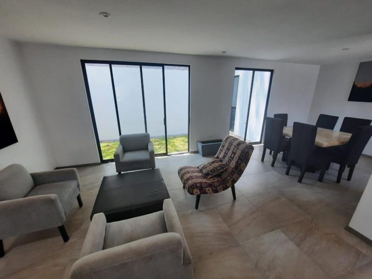 Sala y comedor integrados con ventanales corredizos de cristal, sillones grises y piso cerámico