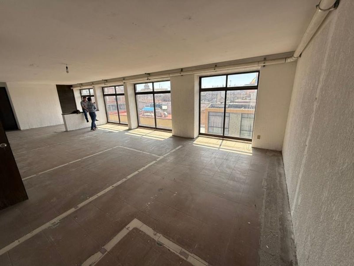 Espacio interior desocupado con piso de azulejo, ventanales con marcos oscuros y paredes blancas