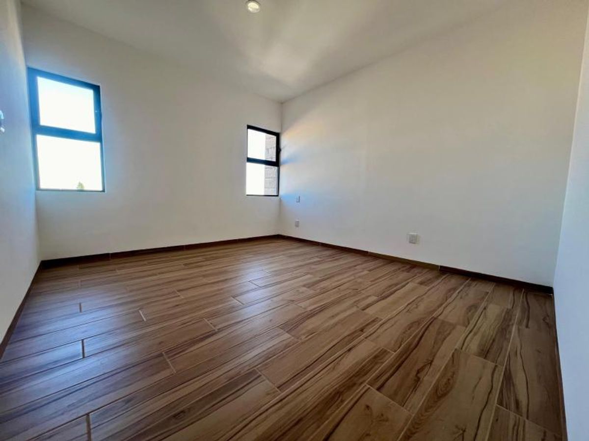 Habitación vacía con paredes blancas, piso tipo madera y dos ventanas con marcos negros