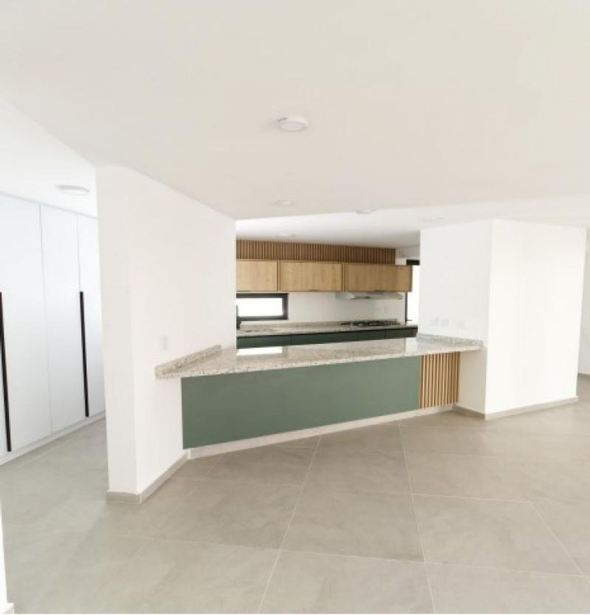 Cocina abierta con barra de granito, gabinetes verdes, alacenas de madera y piso beige