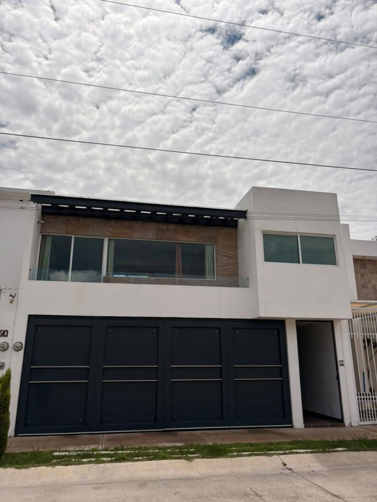 Fachada moderna de dos niveles con portón gris oscuro y ventanales en planta alta