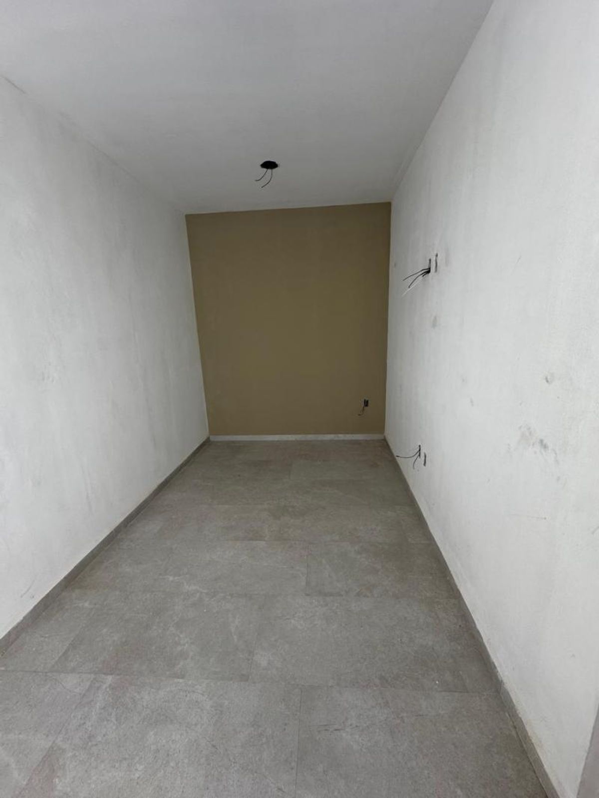 Habitación vacía con piso cerámico gris paredes laterales blancas y pared de fondo café