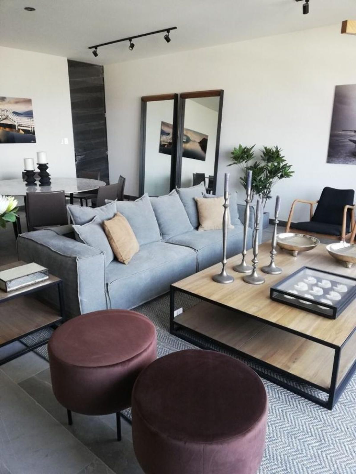 Sala con sofá gris, mesa de centro de madera, pufs de terciopelo y espejos