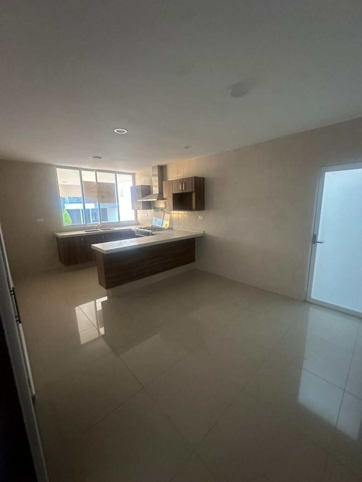 Cocina abierta con gabinetes de madera oscura, barra desayunadora, cubiertas blancas y piso brillante