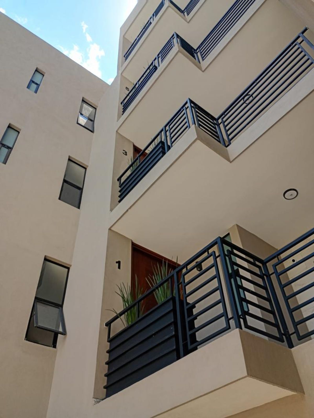 Fachada exterior beige con balcones de herrería negra y ventanas rectangulares de marco oscuro
