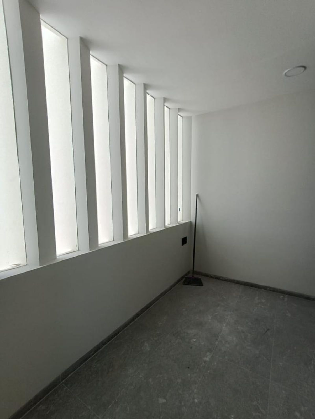 Espacio con paredes blancas, piso de loseta gris y ventanales verticales de vidrio esmerilado