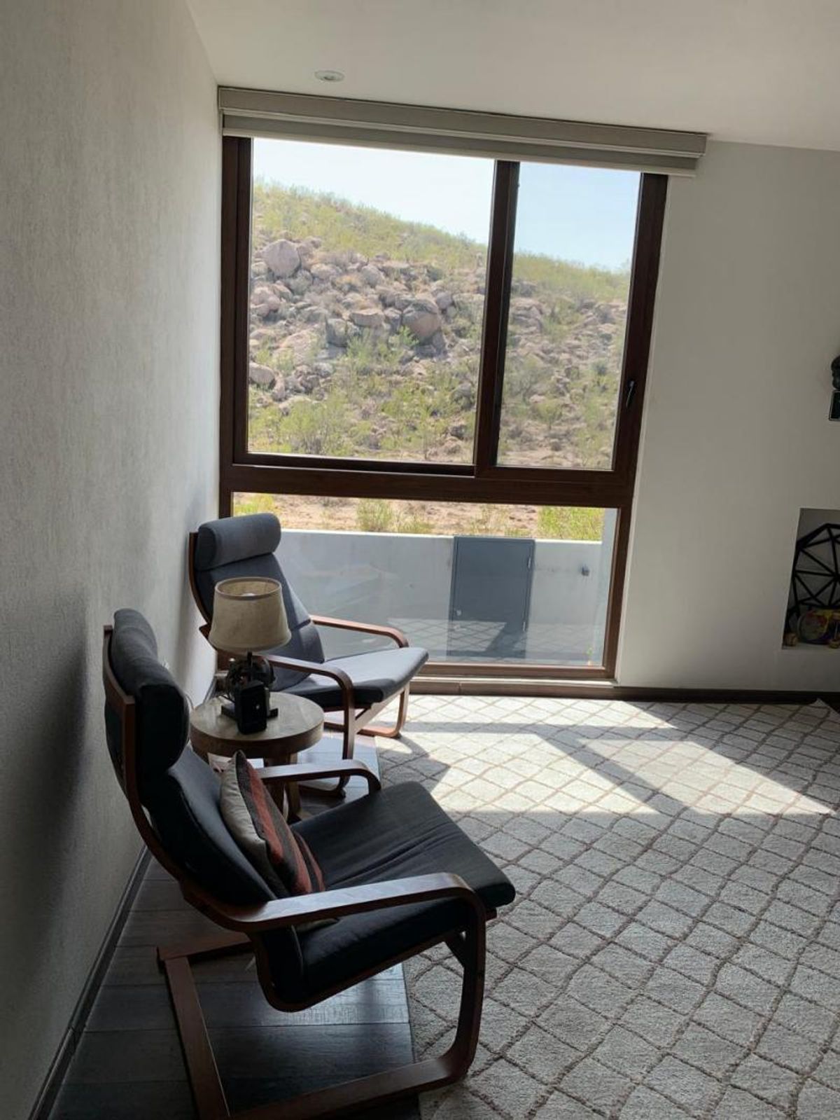 Dos sillones de madera con cojines oscuros junto a ventanal hacia paisaje rocoso