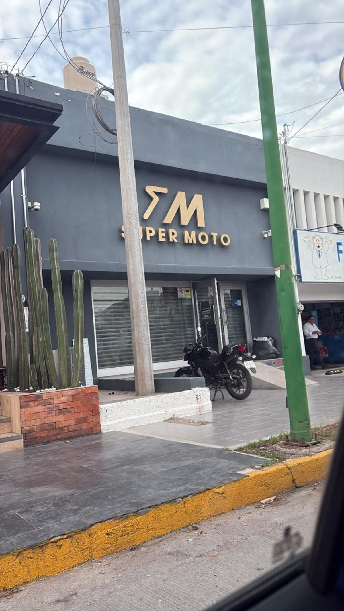 Fachada gris de local comercial con letrero dorado, acceso de cristal y jardinera con cactus