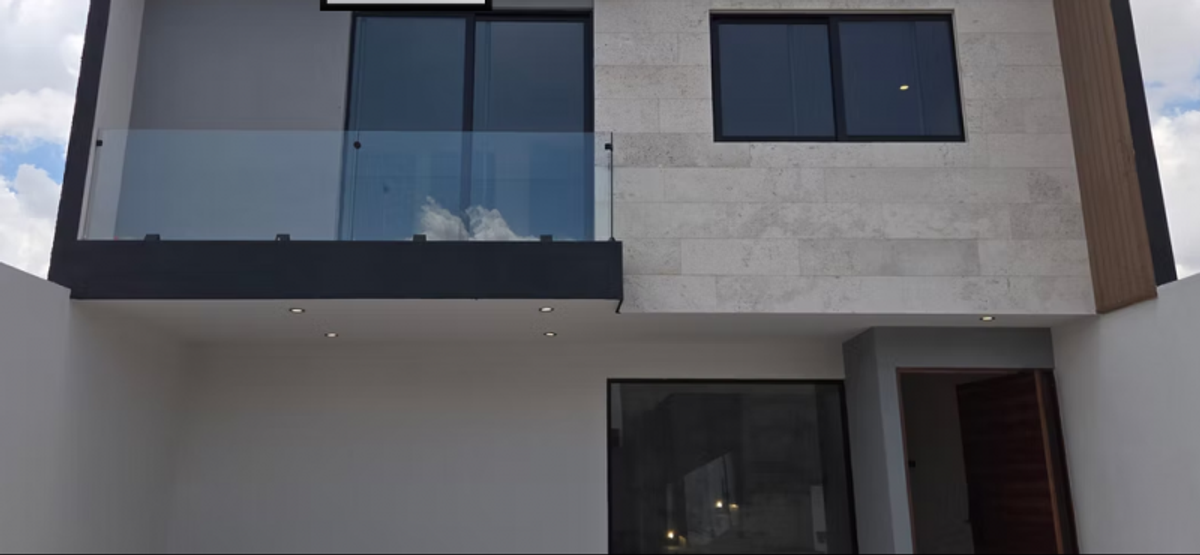 Fachada de dos niveles con balcón de cristal, revestimiento de piedra e iluminación empotrada