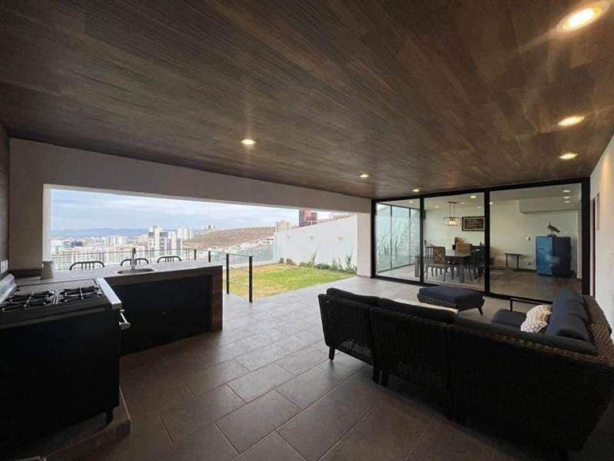 Terraza cubierta con techo de madera, área de cocina, sofás de exterior y ventanales