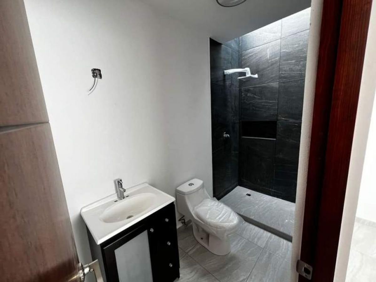 Baño con mueble de lavabo negro, inodoro blanco y ducha revestida con azulejos oscuros