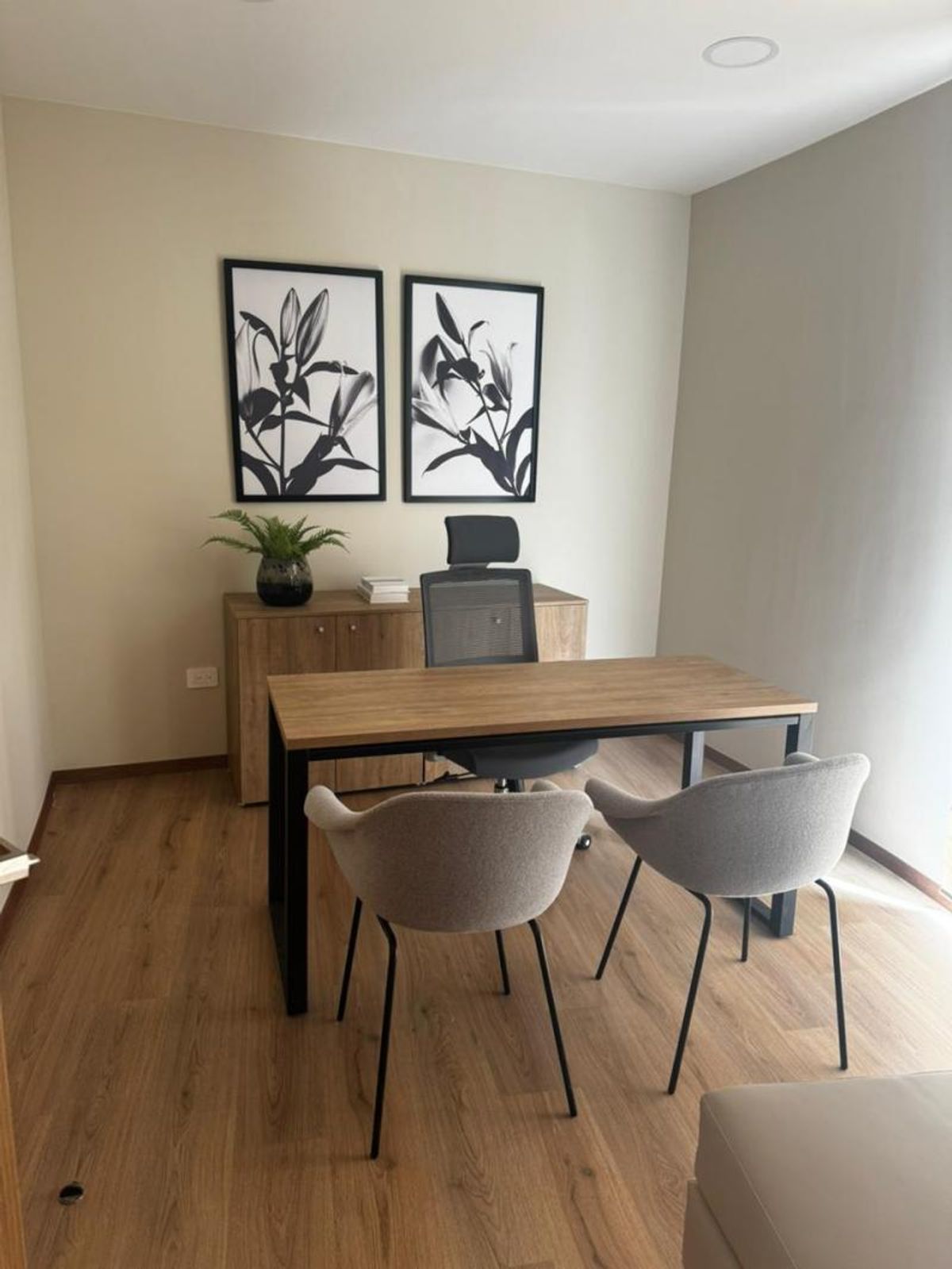 Consultorio con escritorio de madera, sillas tapizadas, credenza al fondo y piso de madera