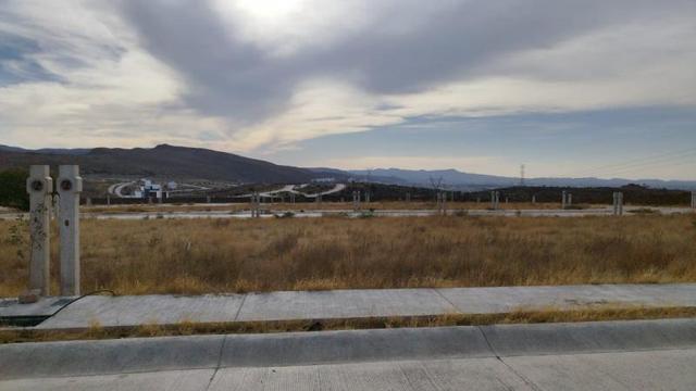 Terreno plano con pasto seco, banqueta de concreto, postes de concreto y montañas al fondo
