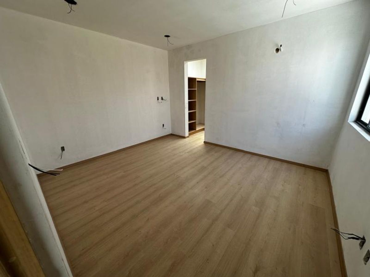 Habitación vacía con piso laminado tono madera clara, paredes blancas y acceso a vestidor