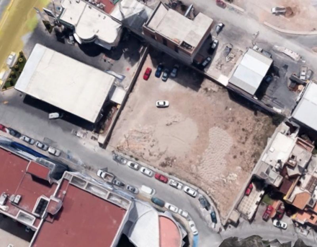 Terreno plano sin construir rodeado de edificaciones comerciales y calles pavimentadas con vehículos estacionados