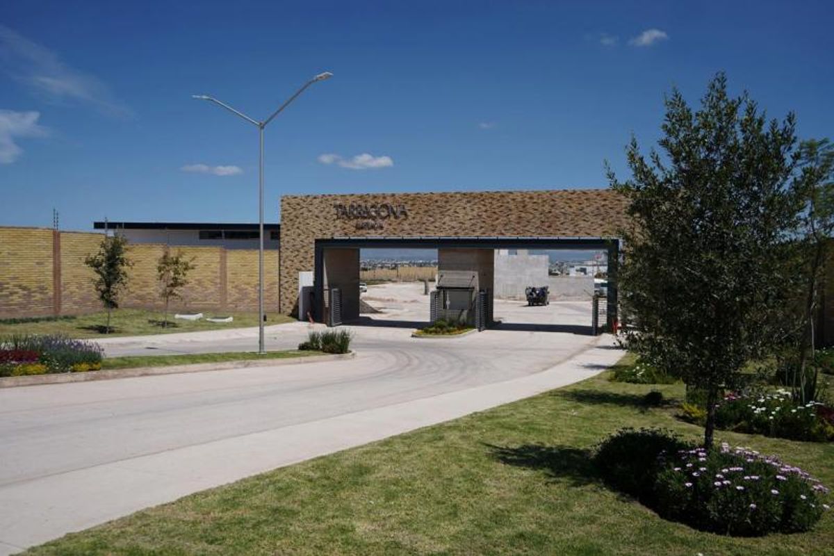 Acceso a residencial con fachada de piedra, calle pavimentada, luminaria exterior y áreas verdes