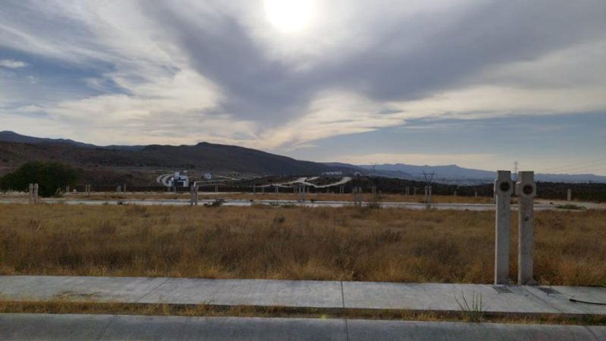 Terreno llano con pasto seco, banquetas de concreto y cerros al fondo