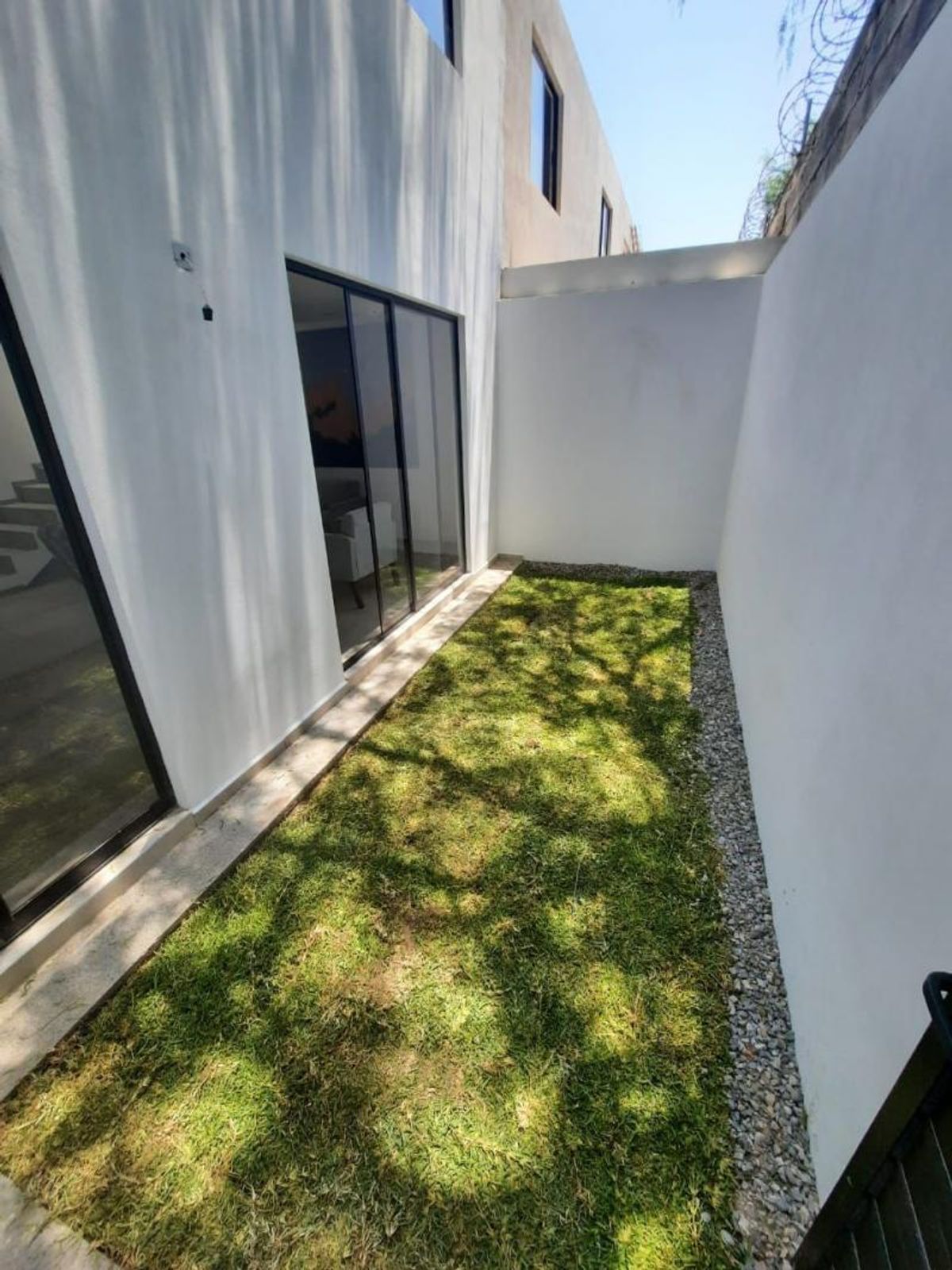 Jardín con pasto verde, borde de grava, muros blancos y puertas corredizas de cristal