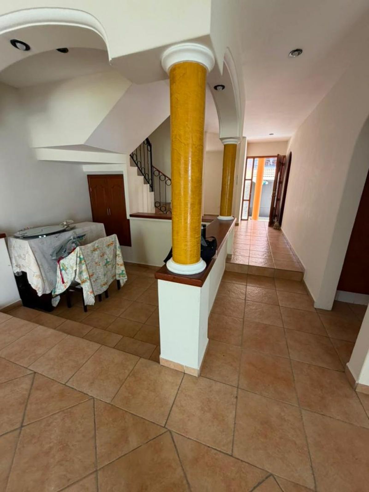 Pasillo interior con piso de cerámica, columnas amarillas sobre murete y escaleras al fondo