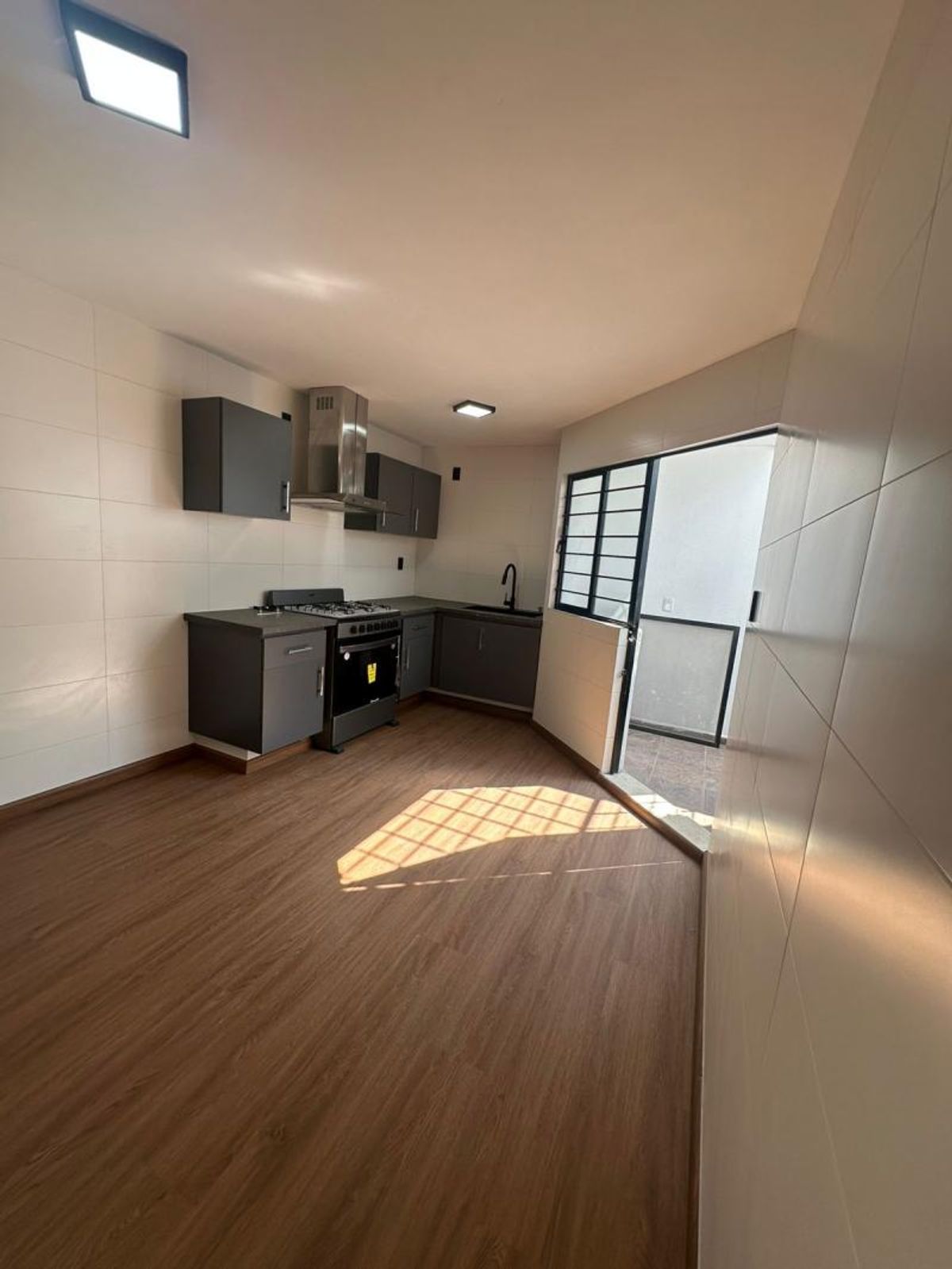 Cocina integral con gabinetes grises, estufa con campana, piso tipo madera y acceso al patio