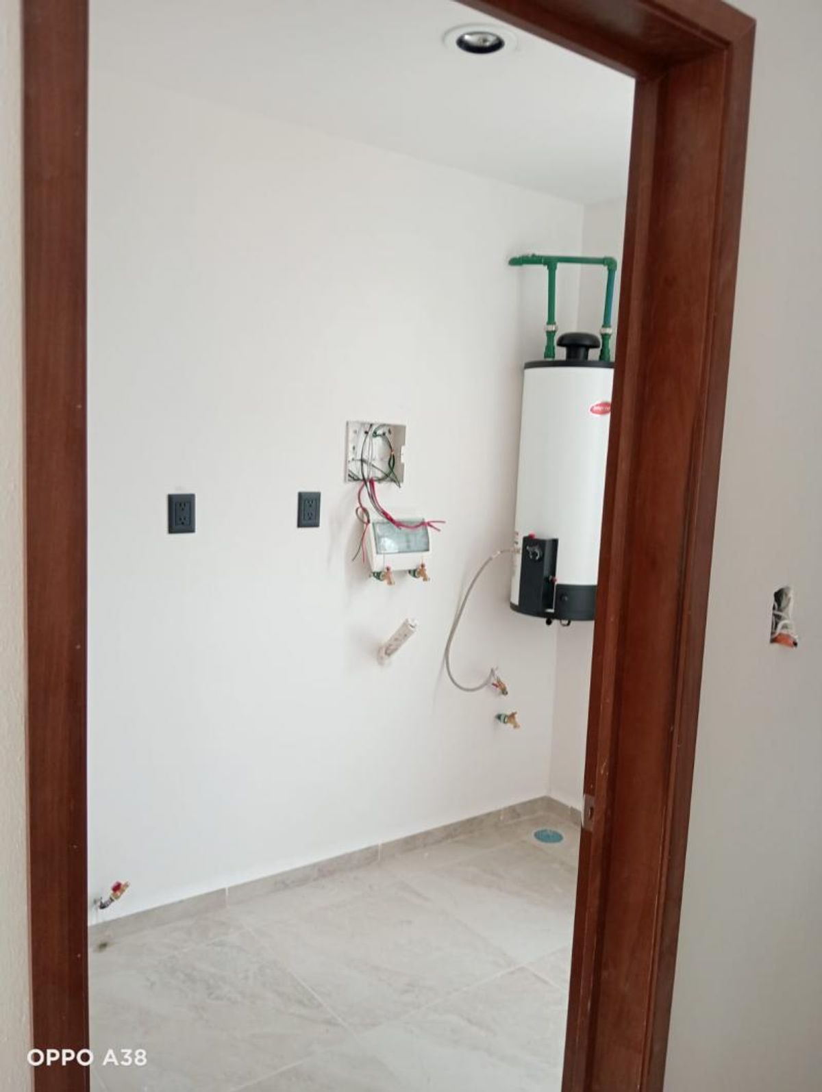 Cuarto de servicio con calentador de agua, piso cerámico gris y conexiones de plomería
