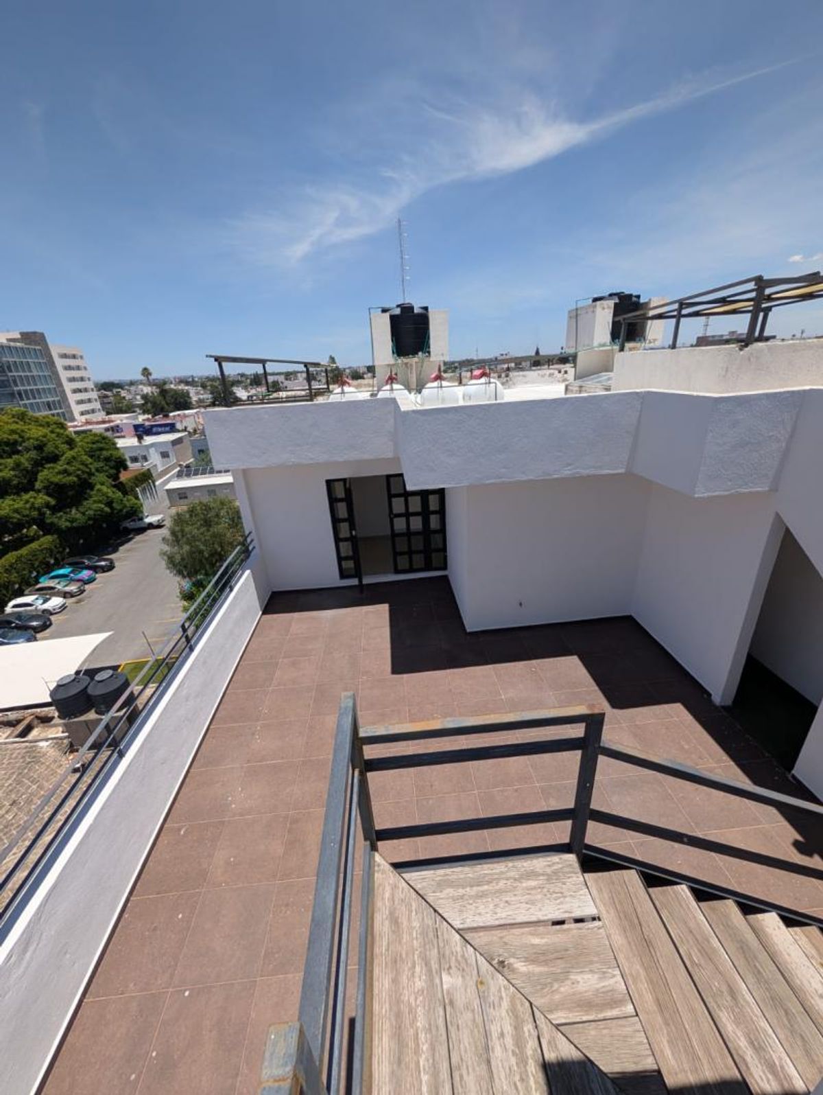 Terraza en azotea con piso de loseta marrón, escaleras de madera y barandales metálicos