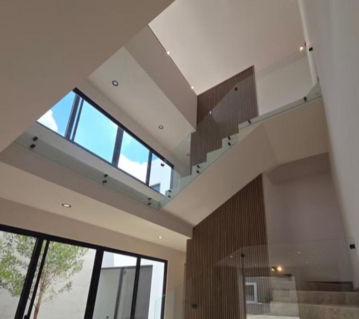 Interior a doble altura con barandales de cristal, panel de madera y grandes ventanales