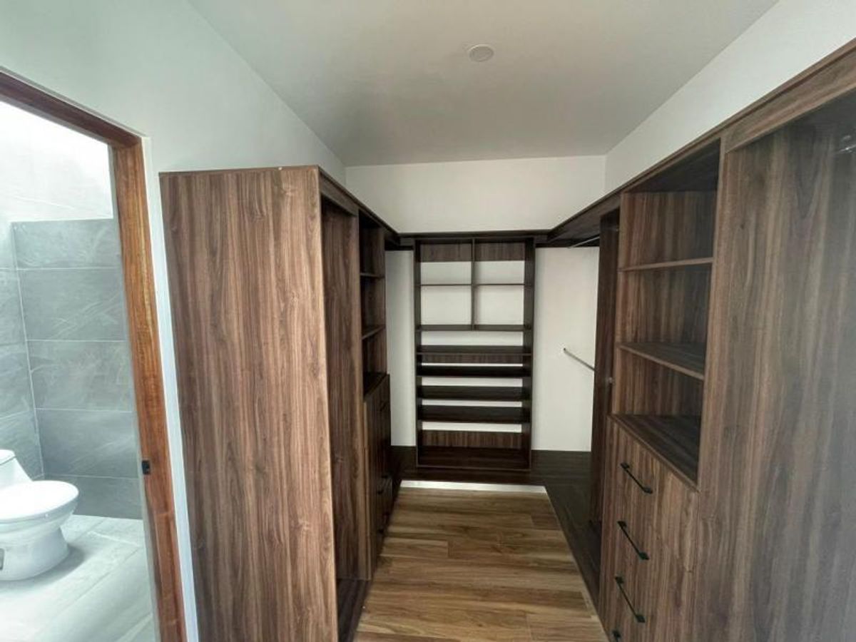 Vestidor de madera oscura con cajoneras, repisas abiertas y piso laminado junto al baño
