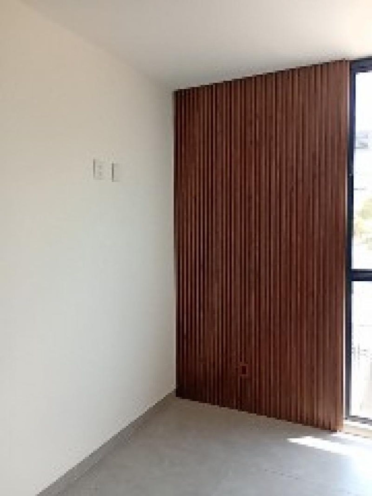 Habitación con pared revestida de listones de madera, muro blanco y piso gris