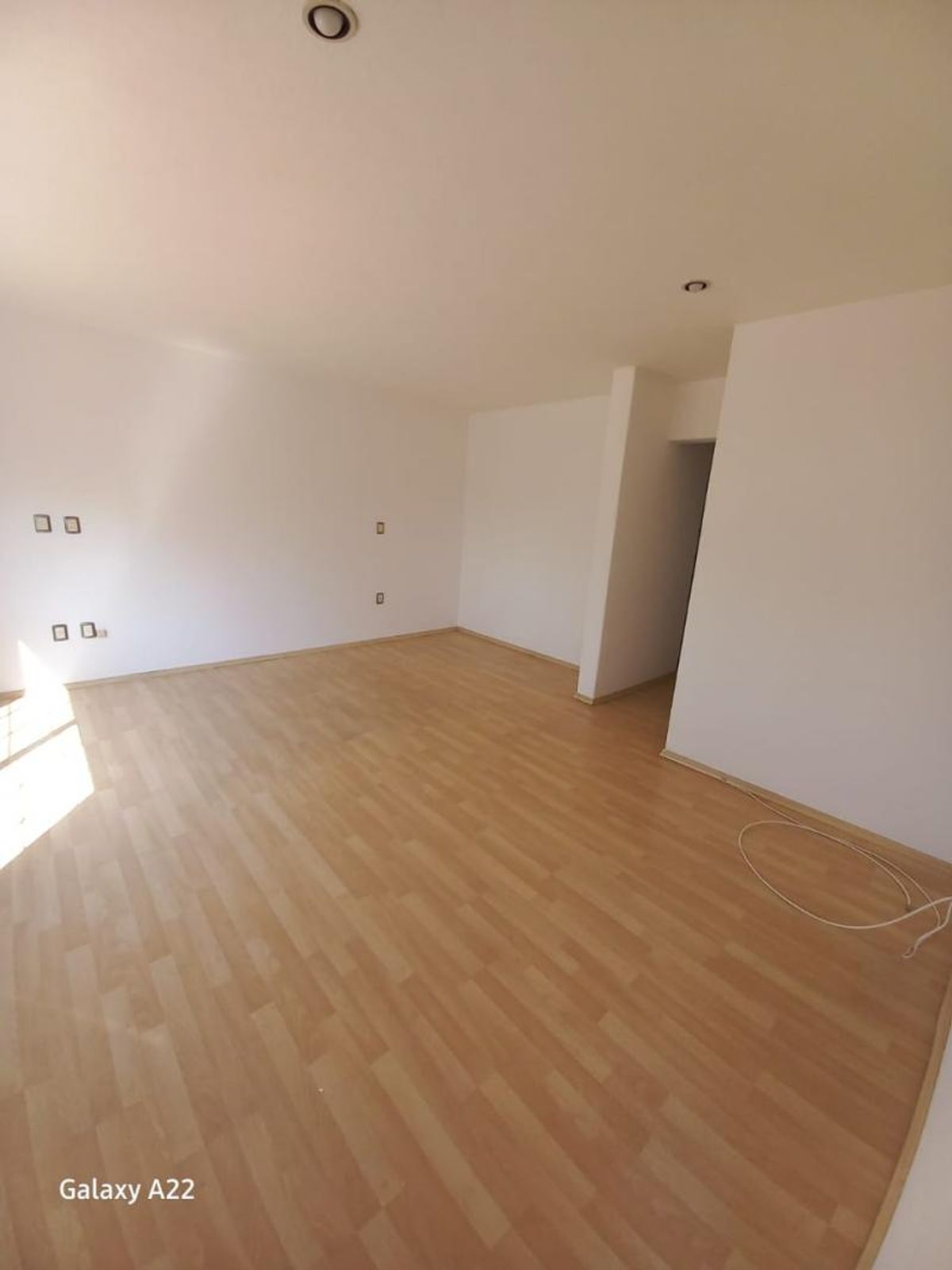 Habitación vacía con piso laminado de madera, paredes blancas e iluminación empotrada