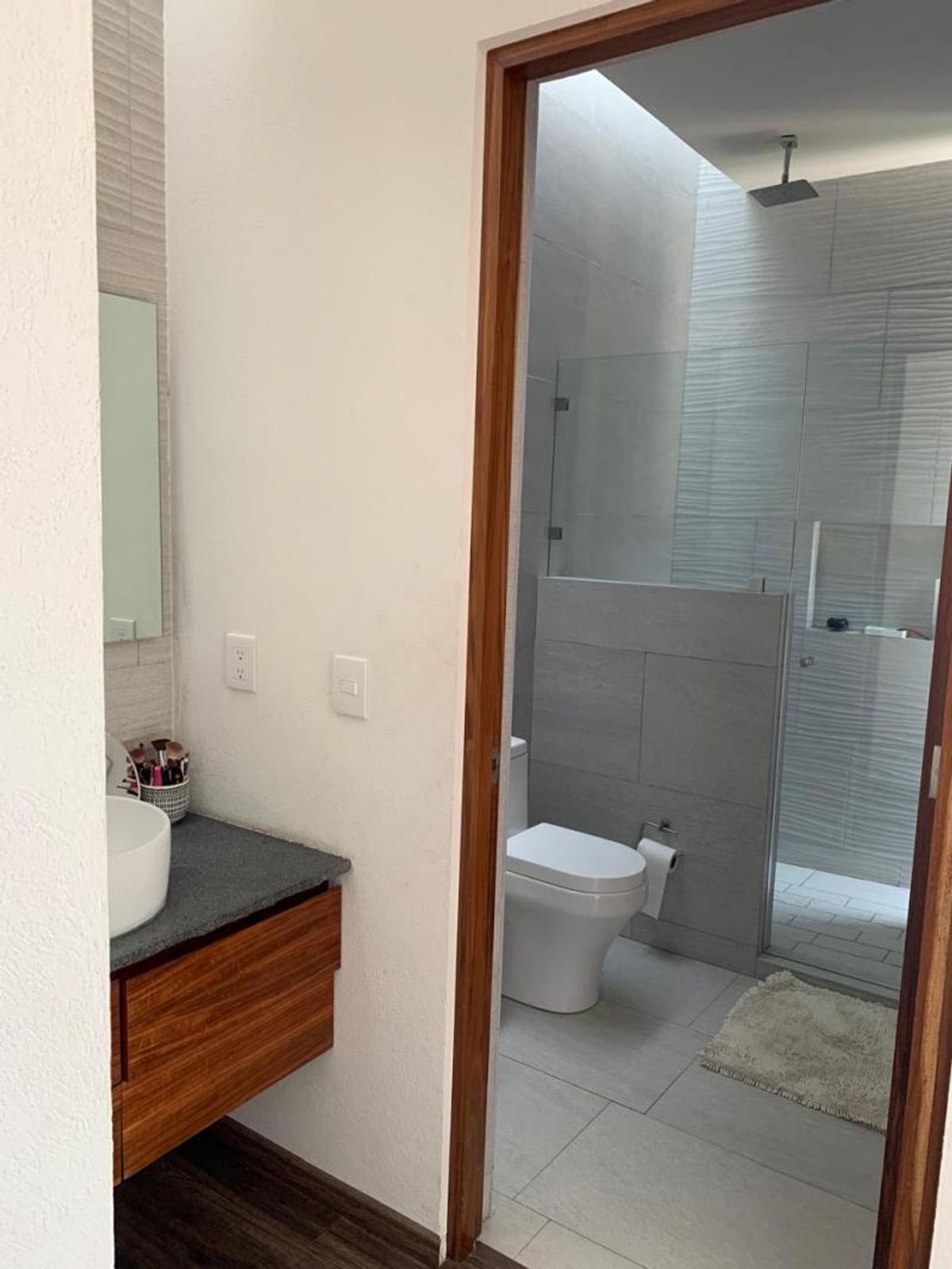 Baño con lavabo sobre mueble de madera, sanitario blanco y regadera con tragaluz