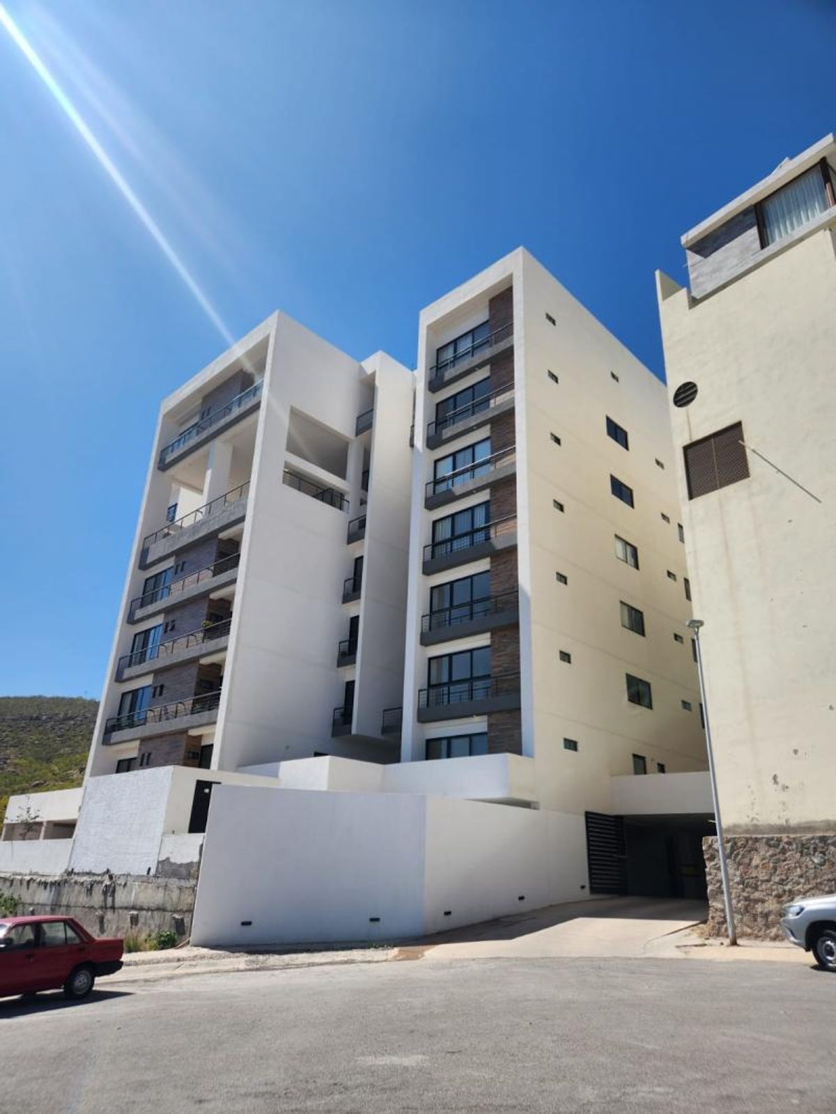 Edificio residencial moderno de varios niveles con fachada blanca, balcones oscuros y acceso vehicular