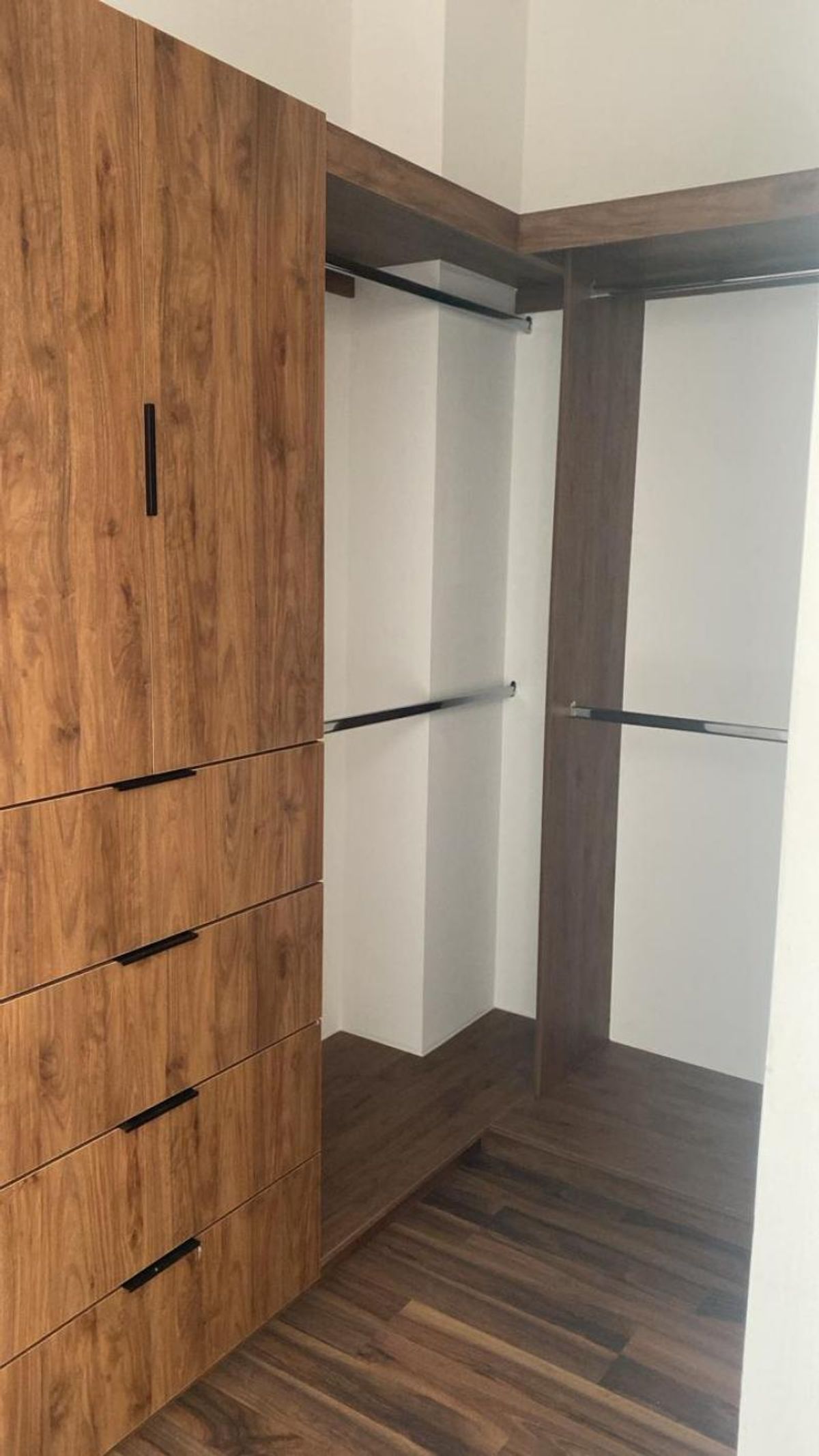 Vestidor de madera con cajoneras, jaladeras negras, tubos metálicos para colgar y piso laminado