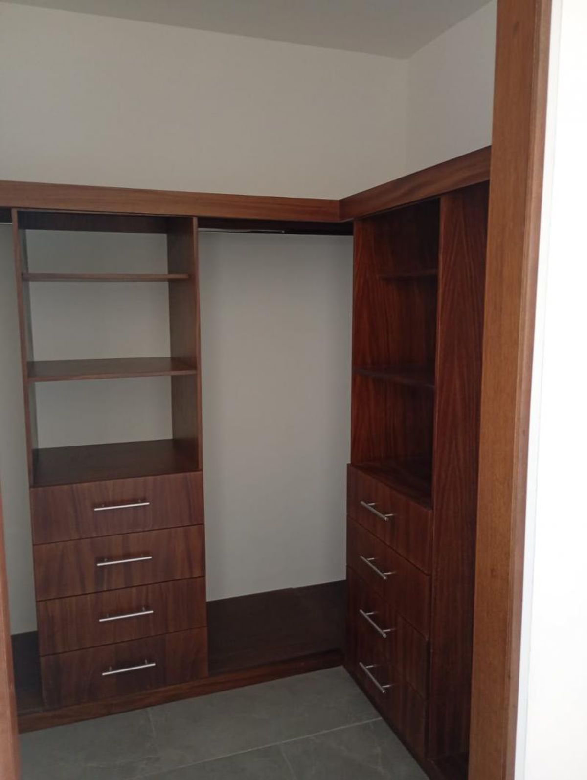 Vestidor de madera con repisas abiertas, cajones con tiradores metálicos y piso gris