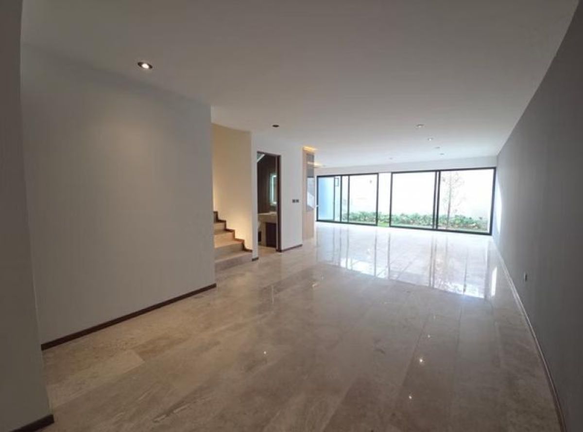 Sala abierta con piso de mármol, luces empotradas y ventanales hacia un jardín