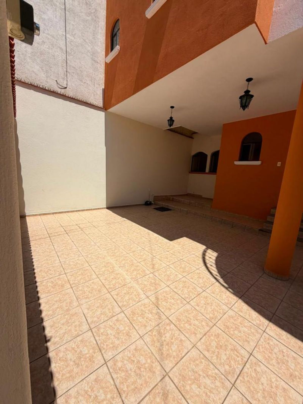 Patio techado con piso de cerámica beige, muros terracota y lámparas colgantes tipo farol