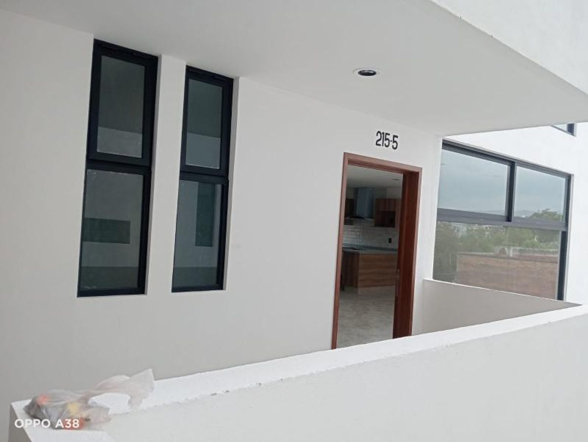 Entrada de departamento con paredes blancas, puerta de madera y ventanas de marco negro