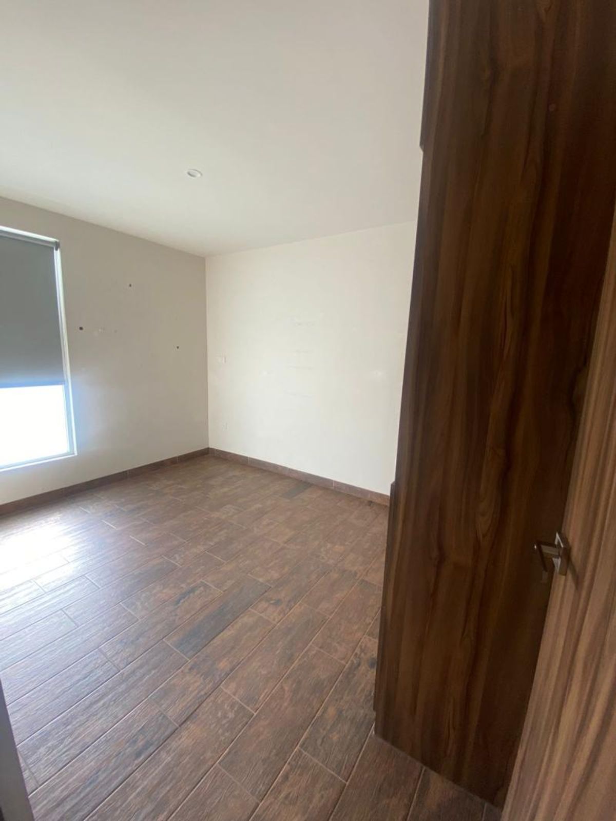 Habitación vacía con piso cerámico tipo madera, paredes claras y ventana con persiana enrollable