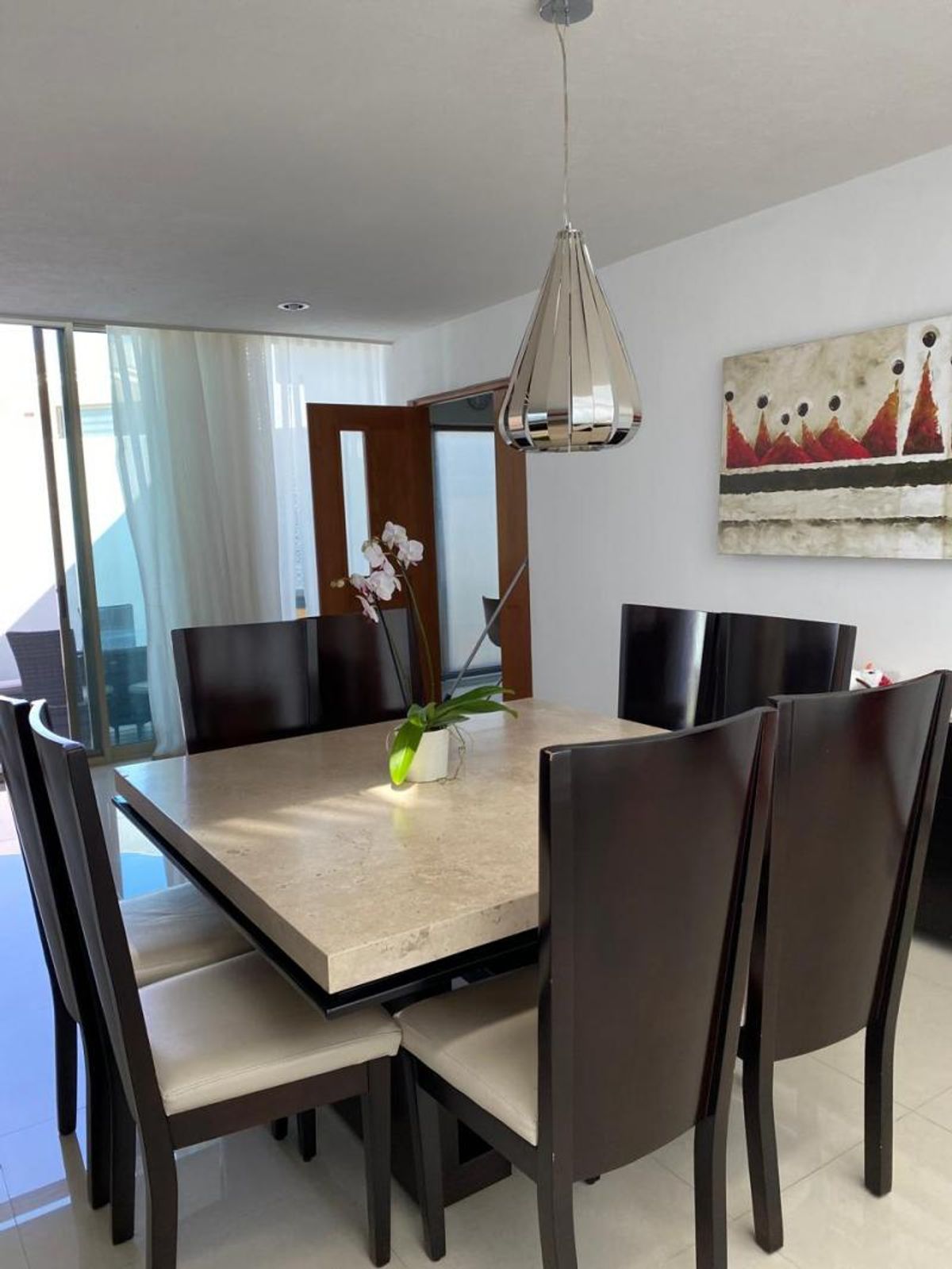 Comedor con mesa de mármol beige, sillas de madera oscura y lámpara colgante metálica