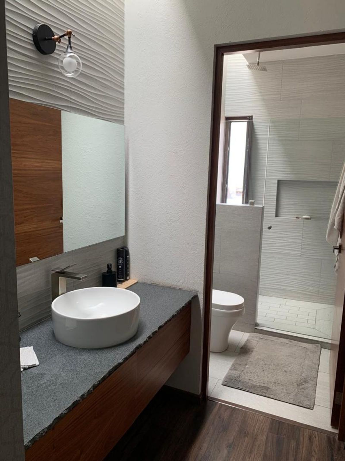 Baño con lavabo de tazón sobre cubierta de granito, mueble de madera y regadera