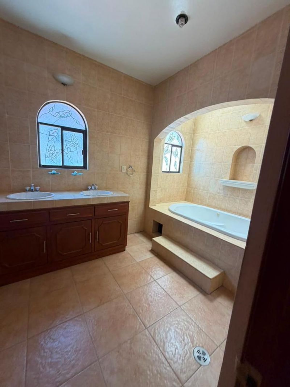 Baño con paredes y piso de azulejo, mueble de madera con doble lavabo y tina