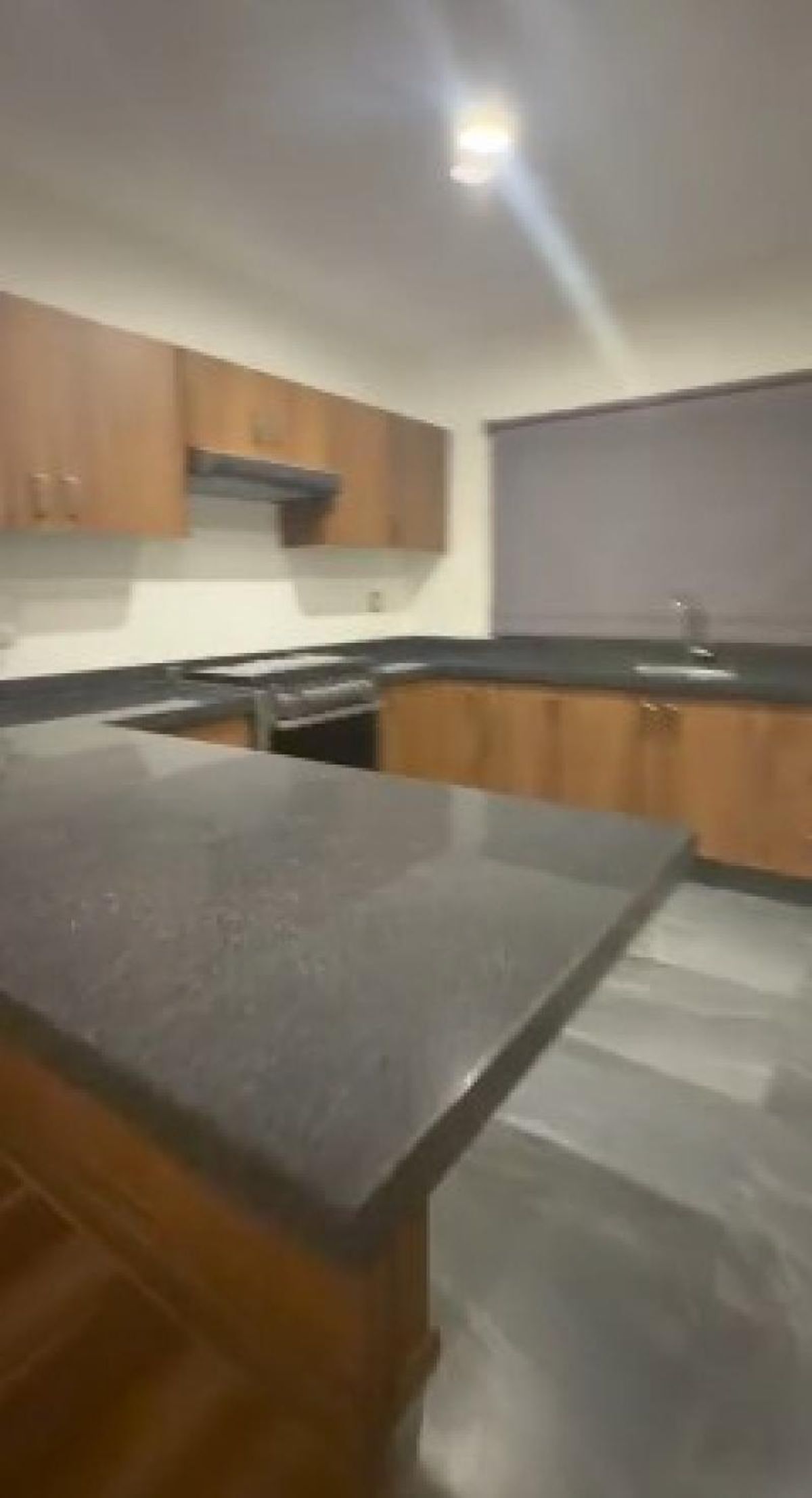 Cocina integral con barra de granito oscuro, gabinetes de madera y ventana con persiana
