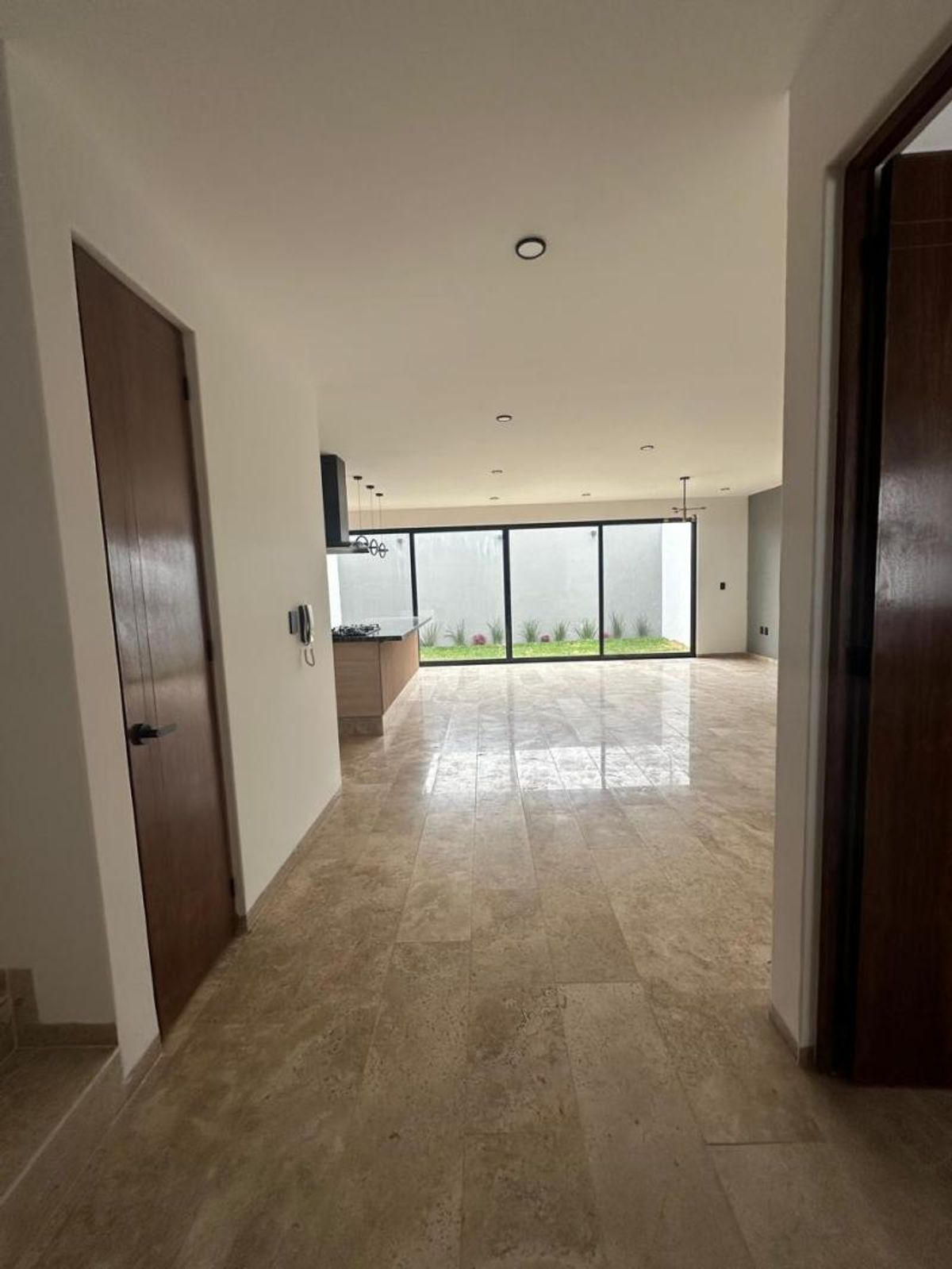 Pasillo con piso de mármol y puertas de madera hacia área con ventanales al jardín