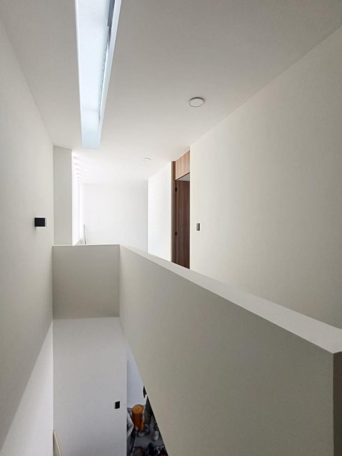 Pasillo superior con murete blanco, tragaluz en el techo y puerta de madera al fondo