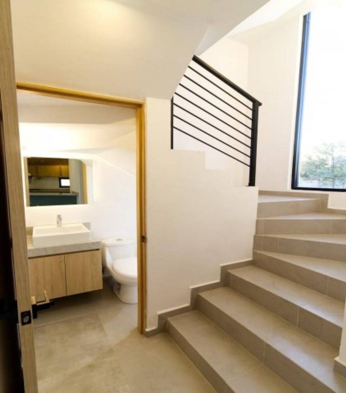Escalera de azulejo beige con barandal negro junto a baño con mueble de madera