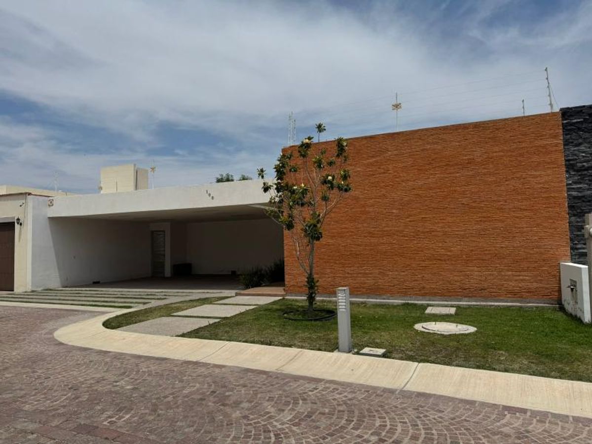 Fachada de un nivel con muro texturizado color naranja, cochera techada y jardín frontal