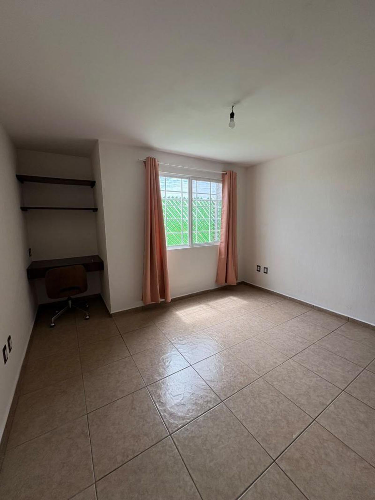Habitación vacía con piso de cerámica, ventana con cortinas y escritorio empotrado con repisas