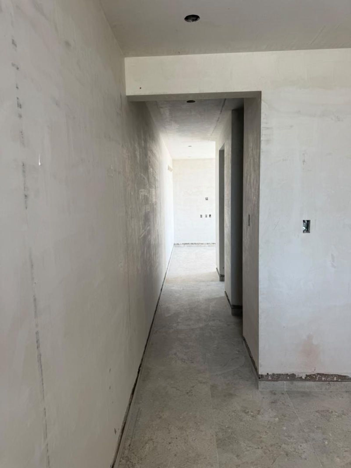 Pasillo interior en obra blanca con piso cerámico gris y muros enyesados