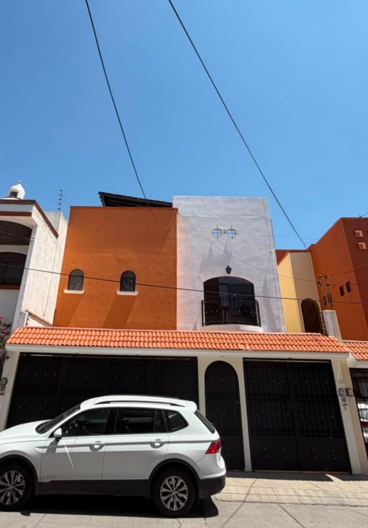 Fachada color terracota y blanco con teja roja, portón negro y camioneta blanca estacionada